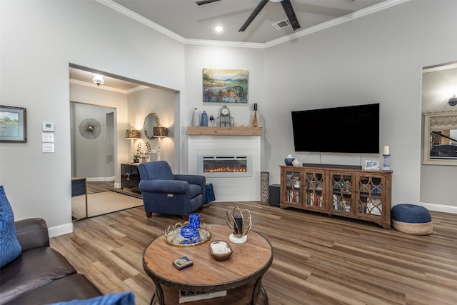 living room featuring a warm lit fireplace, visible vents, baseboards, ornamental molding, and wood finished floors