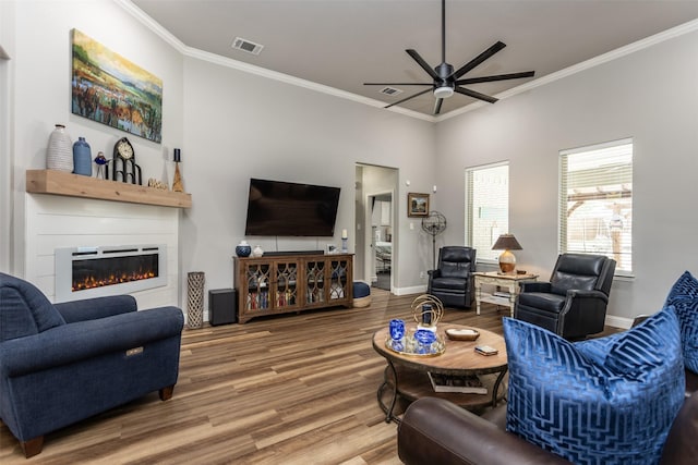 living area featuring wood finished floors, visible vents, baseboards, ornamental molding, and a glass covered fireplace