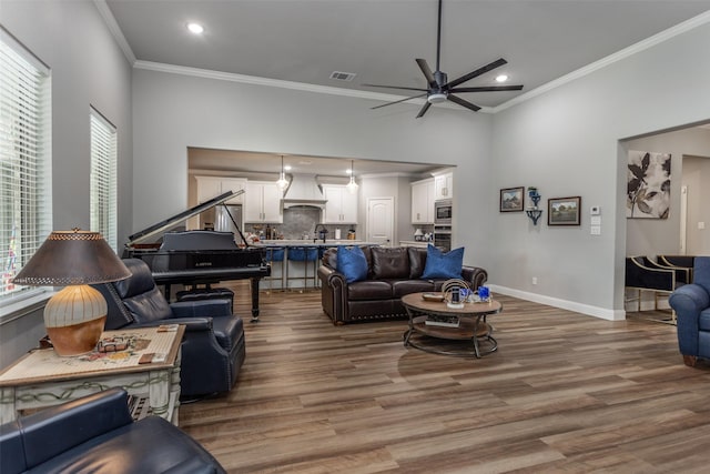 living area featuring visible vents, ornamental molding, a ceiling fan, wood finished floors, and baseboards