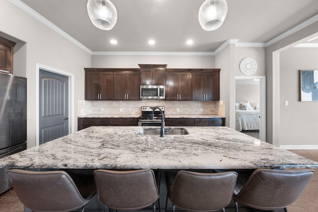 kitchen featuring a large island, appliances with stainless steel finishes, a sink, dark brown cabinets, and backsplash