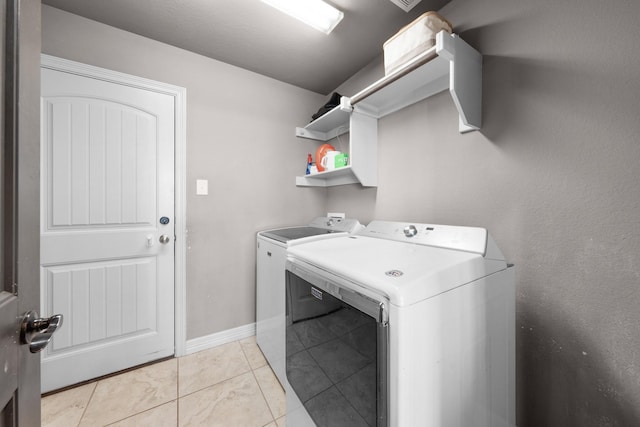 clothes washing area featuring laundry area, washer and clothes dryer, baseboards, and light tile patterned floors