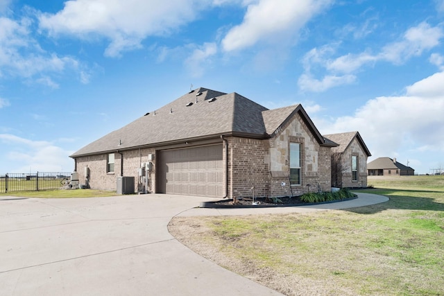 view of front facade with central AC unit, roof with shingles, fence, a front yard, and brick siding