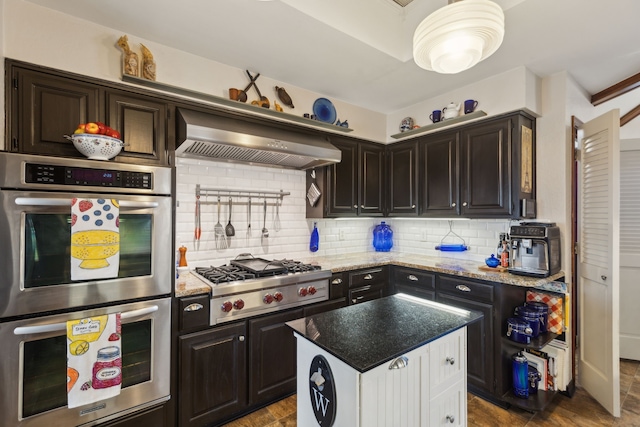 kitchen with backsplash, appliances with stainless steel finishes, dark brown cabinets, light stone countertops, and wall chimney exhaust hood