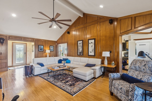 living room featuring wooden walls, ceiling fan, beamed ceiling, light wood-type flooring, and high vaulted ceiling