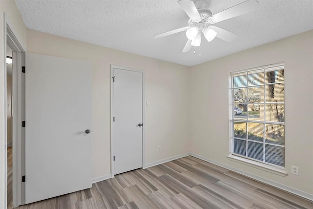 unfurnished bedroom with a ceiling fan, light wood-type flooring, a textured ceiling, and baseboards