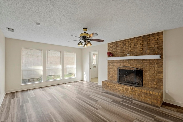 unfurnished living room with visible vents, baseboards, ceiling fan, wood finished floors, and a brick fireplace