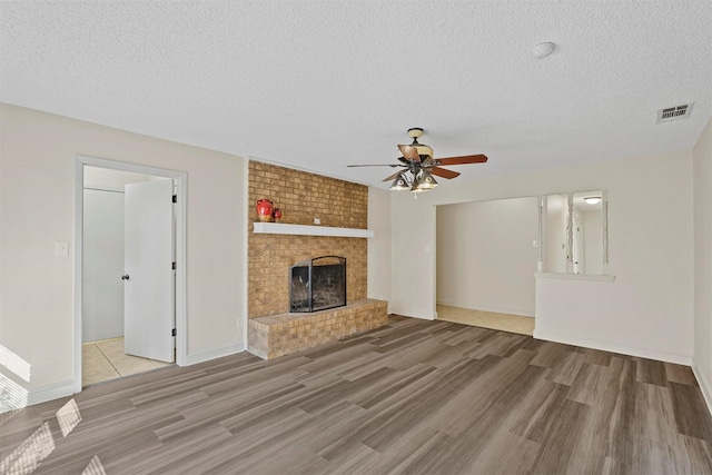 unfurnished living room with baseboards, ceiling fan, wood finished floors, a textured ceiling, and a brick fireplace