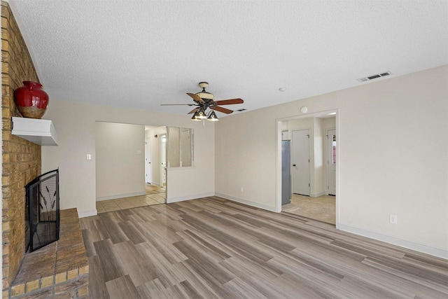 unfurnished living room with light wood-style floors, visible vents, a fireplace, and a textured ceiling