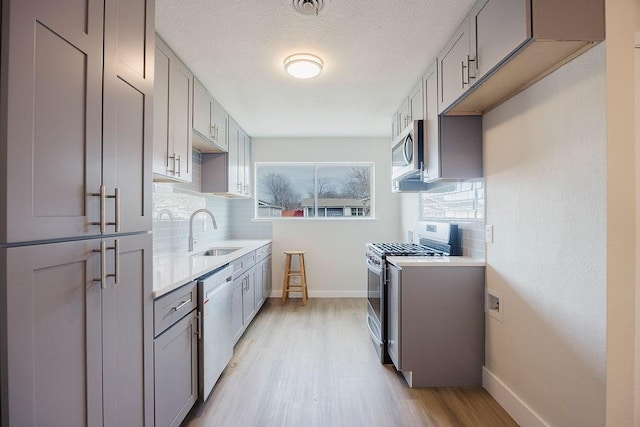 kitchen featuring stainless steel appliances, tasteful backsplash, gray cabinets, light countertops, and a sink