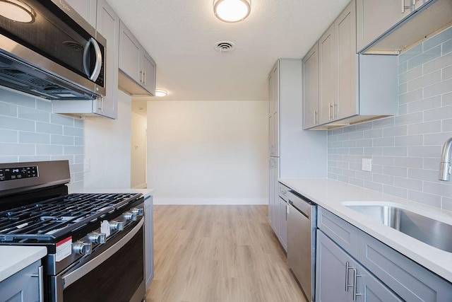 kitchen featuring stainless steel appliances, a sink, light countertops, and gray cabinetry