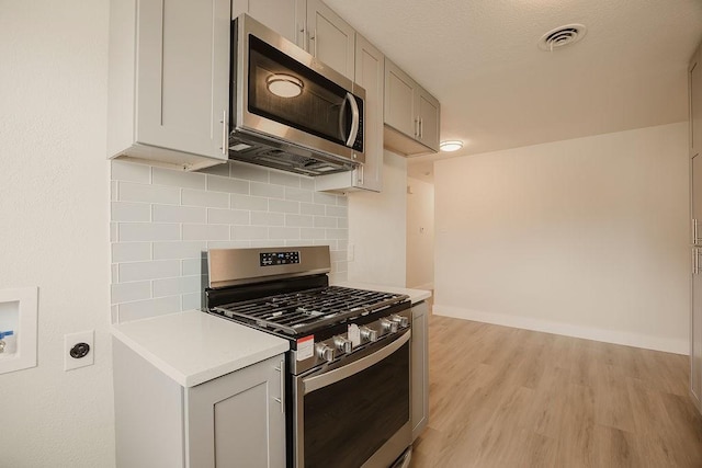 kitchen featuring stainless steel appliances, visible vents, light wood-style floors, light countertops, and decorative backsplash