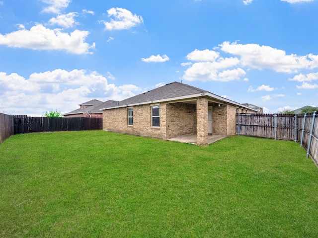 rear view of house with brick siding, a yard, a patio, a shingled roof, and a fenced backyard