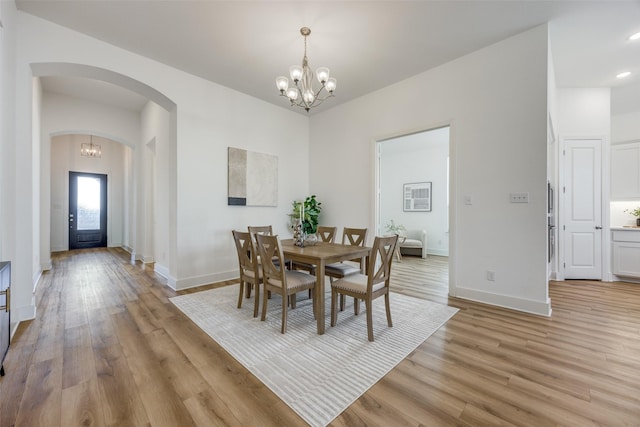 dining space featuring light wood-style flooring, a chandelier, and arched walkways