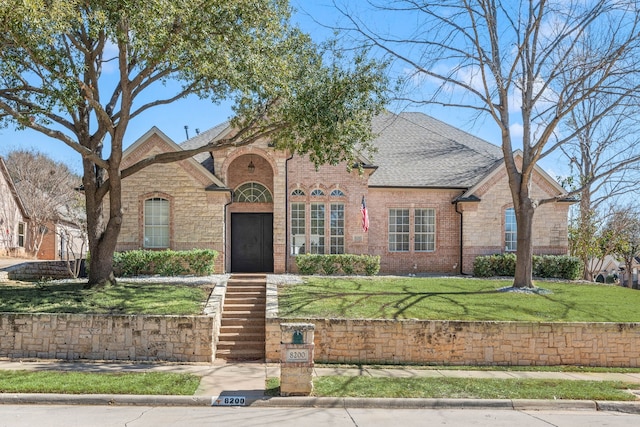 view of front of home featuring stone siding, a shingled roof, a front yard, and brick siding