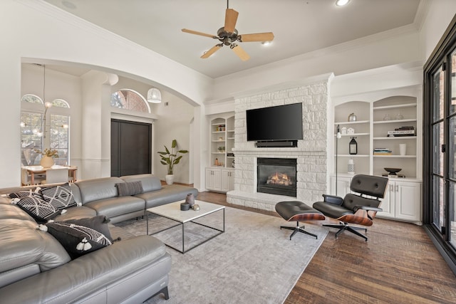 living area with built in shelves, crown molding, a fireplace, a ceiling fan, and wood finished floors