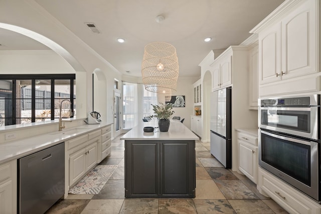 kitchen with stainless steel appliances, a sink, white cabinetry, ornamental molding, and a center island