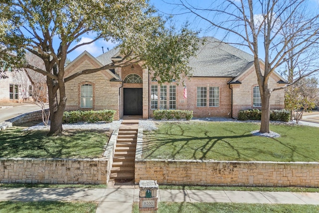 french country style house featuring brick siding, roof with shingles, and a front yard