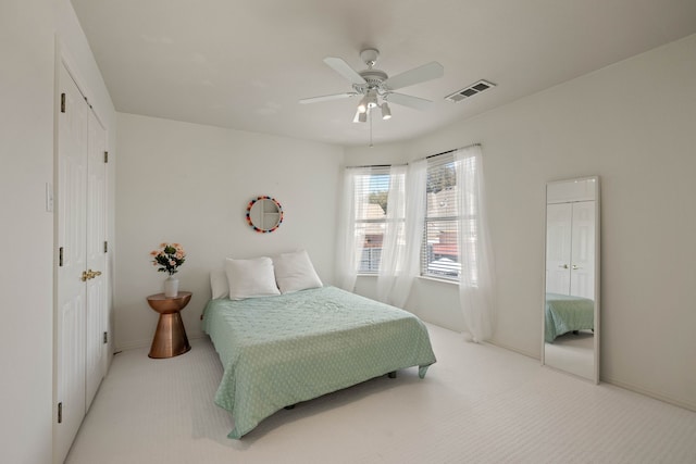 bedroom featuring a ceiling fan, a closet, visible vents, and light colored carpet