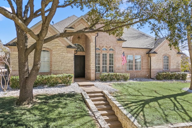 french country home with a front lawn, roof with shingles, and brick siding