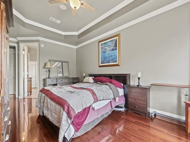 bedroom featuring wood finished floors, visible vents, baseboards, ornamental molding, and a tray ceiling