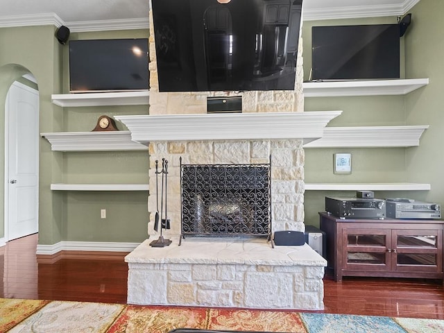 interior details featuring baseboards, arched walkways, wood finished floors, crown molding, and a fireplace