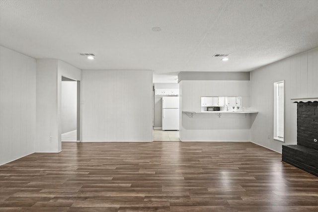 unfurnished living room with a textured ceiling, a fireplace, visible vents, and wood finished floors