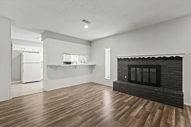 unfurnished living room with a textured ceiling, a brick fireplace, wood finished floors, and visible vents