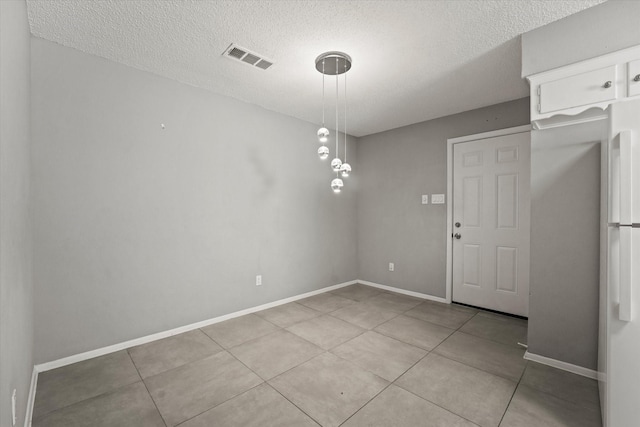 unfurnished dining area with a textured ceiling, tile patterned floors, visible vents, and baseboards