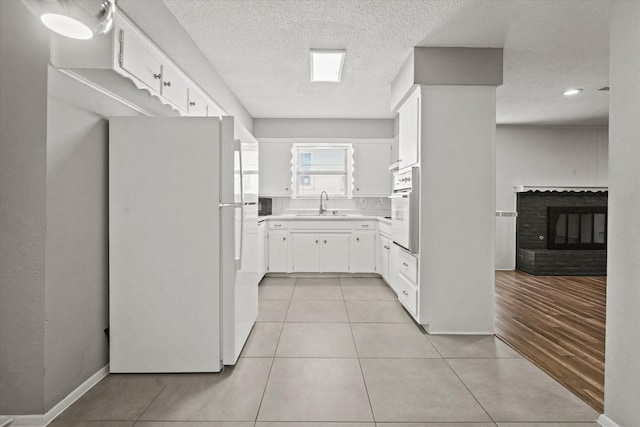 kitchen featuring a brick fireplace, light tile patterned flooring, a sink, white cabinets, and white appliances