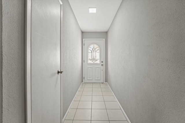 doorway to outside with light tile patterned floors, a textured wall, and baseboards