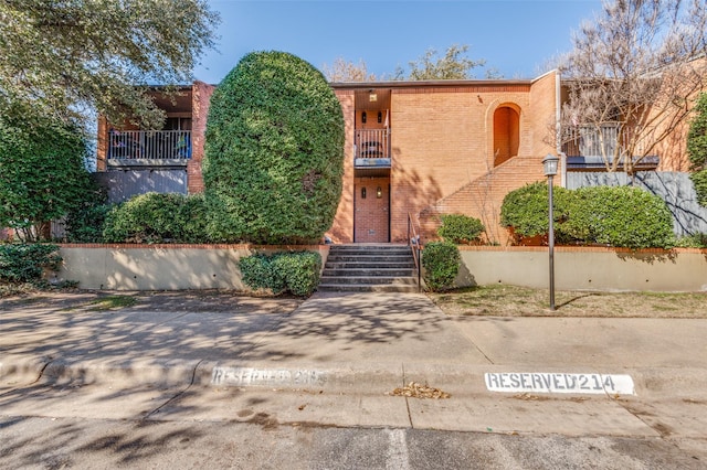 view of front of property featuring a balcony, stairway, and brick siding