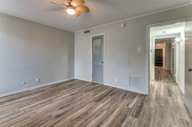 empty room with crown molding, visible vents, ceiling fan, and wood finished floors