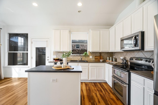 kitchen featuring dark countertops, a kitchen island, stainless steel appliances, and a sink