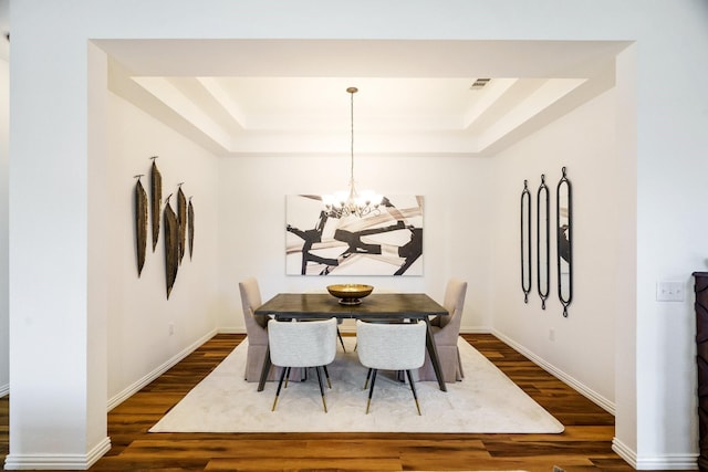 dining space with dark wood-style floors, a tray ceiling, baseboards, and a notable chandelier