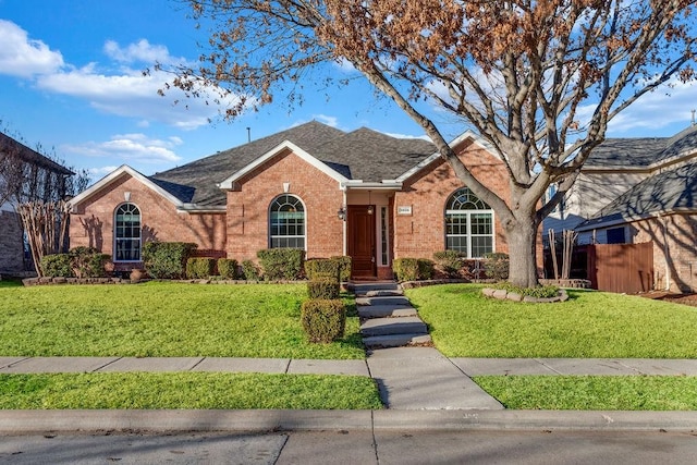 ranch-style home featuring a front yard, fence, brick siding, and roof with shingles