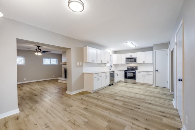 kitchen with a fireplace with raised hearth, appliances with stainless steel finishes, light wood-style floors, and white cabinets