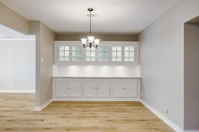 unfurnished dining area with light wood-type flooring, visible vents, baseboards, and an inviting chandelier