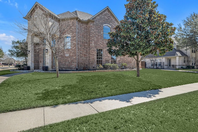 view of front of house with a shingled roof, a front lawn, and brick siding