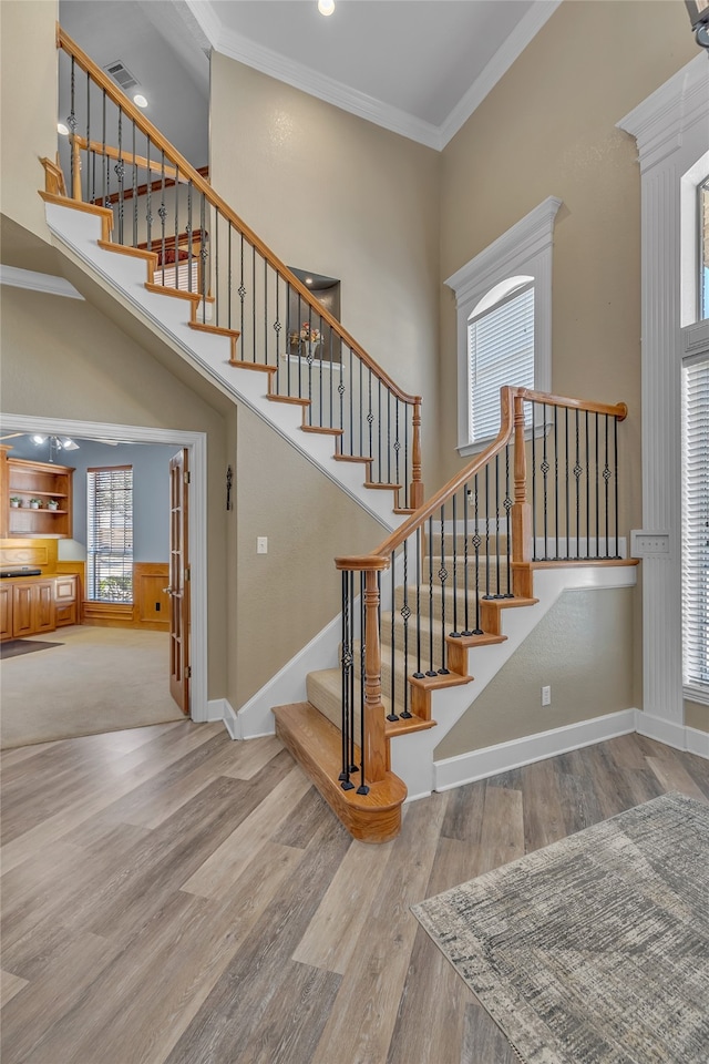 stairs featuring visible vents, ornamental molding, wood finished floors, a high ceiling, and baseboards