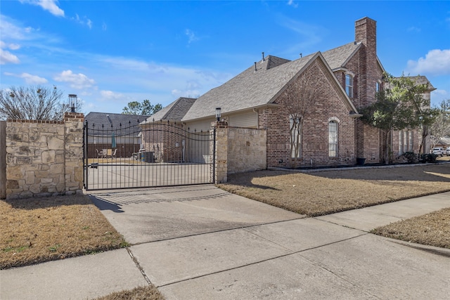 exterior space with a gate, brick siding, a chimney, and roof with shingles