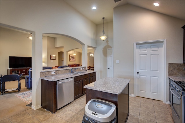 kitchen with arched walkways, light tile patterned flooring, dark brown cabinetry, a sink, and appliances with stainless steel finishes