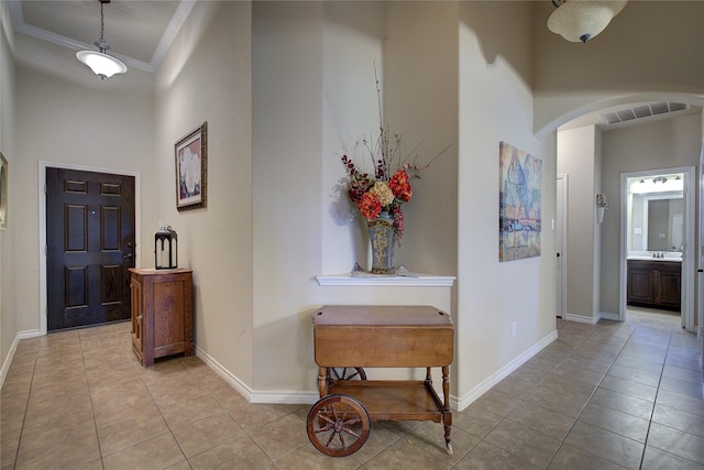 hallway featuring arched walkways, visible vents, a high ceiling, ornamental molding, and baseboards