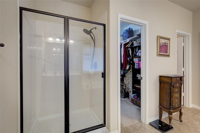 bathroom with a walk in closet, a shower stall, baseboards, and tile patterned floors