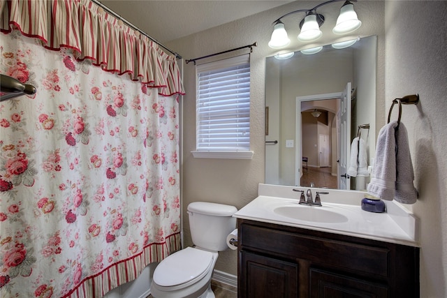 full bath featuring curtained shower, a textured wall, vanity, and toilet