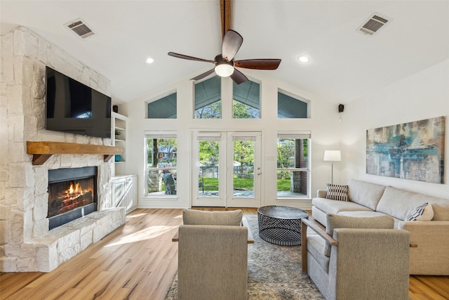 living area with vaulted ceiling, a stone fireplace, wood finished floors, and visible vents