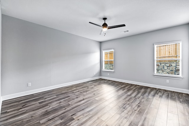 spare room with baseboards, ceiling fan, visible vents, and dark wood-style flooring