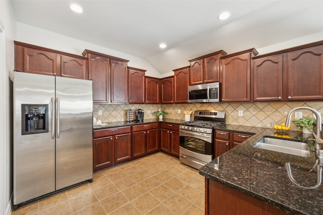 kitchen with lofted ceiling, decorative backsplash, appliances with stainless steel finishes, a sink, and dark stone countertops