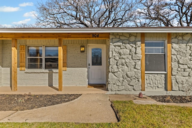 property entrance with covered porch, stone siding, and brick siding