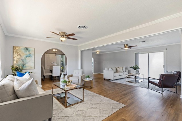 living room featuring arched walkways, ceiling fan, wood finished floors, visible vents, and ornamental molding