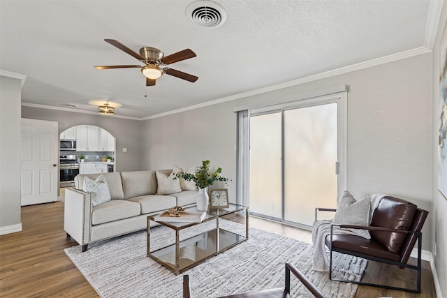 living room featuring arched walkways, visible vents, crown molding, and wood finished floors